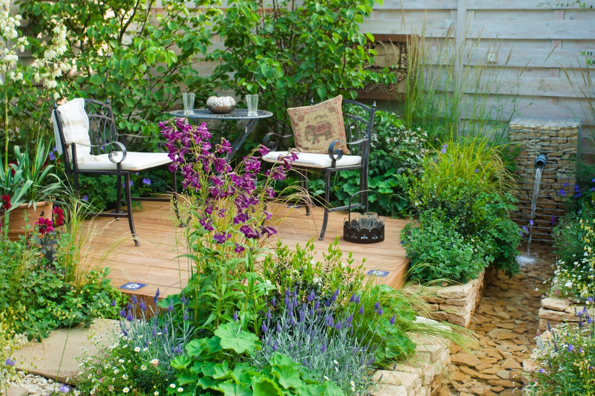 garden seats and table on a small raised patio surrounded by plants